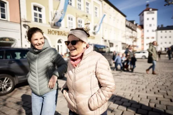 Anna und ihre Mutter Faride gehen untergehakt durch die Innenstadt und lachen.